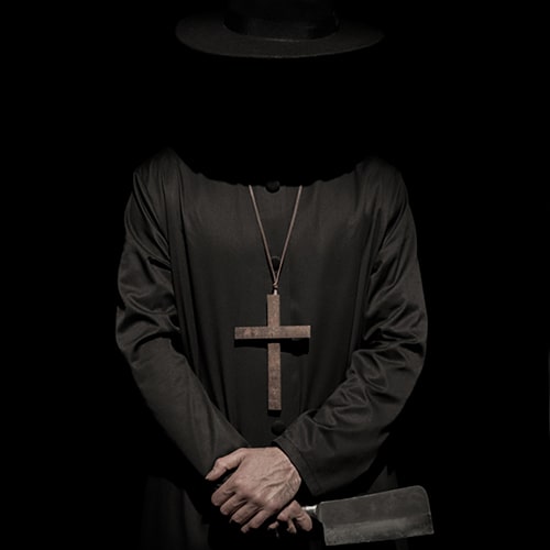 Photo of a faceless figure clothed in a black hat and robe with a wooden cross necklace and a cleaver in his hands  - mahdi rezaei on Unsplash