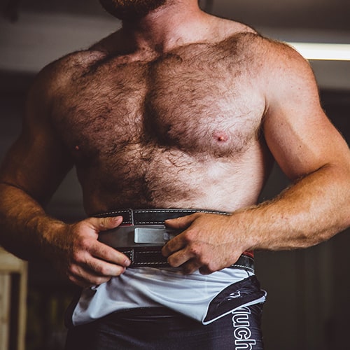 Photo of a shirtless man/weightlifter with his hands on his weight belt, adjusting it - Alora Griffiths on Unsplash