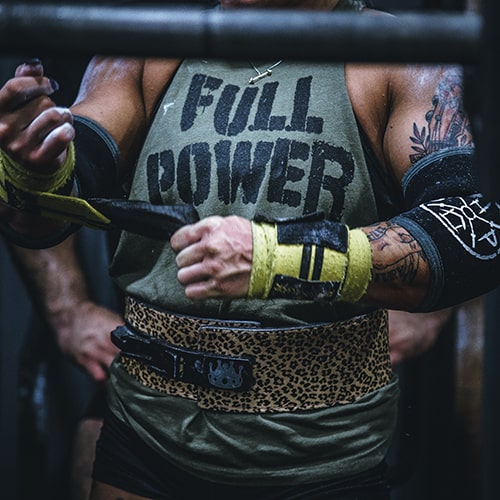 Photo of a weight lifter's torso, who's readjusting his arm guard velcro/tape and wearing other guards, a 'Full Power' sleeveless tank, and a leopard-print body belt - Alora Griffiths on Unsplash