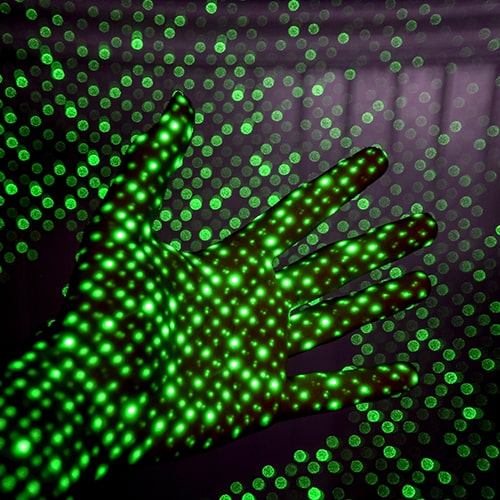 Photo of a dotted laser pointed pattern projecting over someone's hand and along the background wall