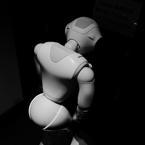 Low-light photo of a white robot with its back turned to the camera, head hung just a bit