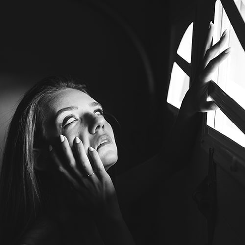 Photo of a 'blind' woman with all-white scleras pulling down on the right side of her face with a hand up to a door window - Alex Iby on Unsplash