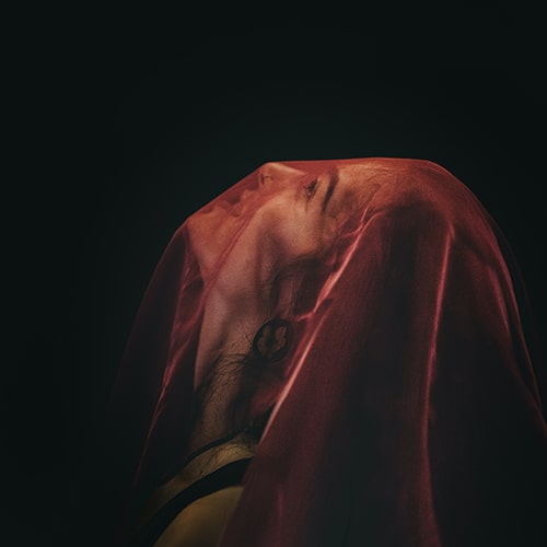 Photo of a woman in a sheer red veil, looking up on a black background - Sandra Seitamaa on Unsplash