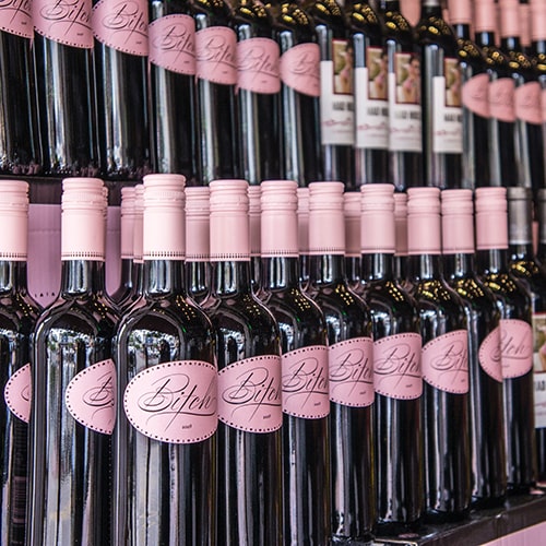 Two rows of 'Bitch Vodka', with a pink cap wrapping and label on display shelving - Andrew Ruiz on Unsplash