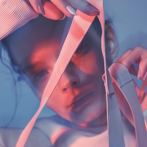 Photo of a woman in pink lighting holding up pink straps to the camera - Igor Rand on Unsplash