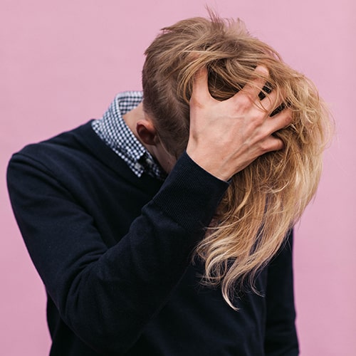 Whimsical shot of a preppy individual running their fingers through their long blond hair (hair styled long in the front and shaved in the back/sides).