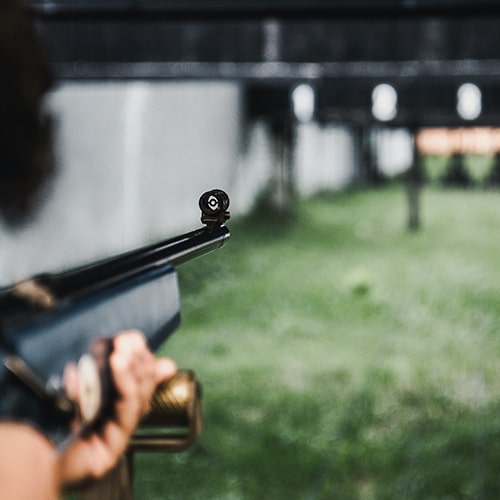 Individual holding a gun with a scope at the end of it, aiming it at targets in the distance at a shooting range.