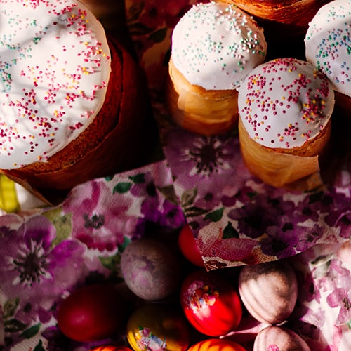 Photo of white-frosted cupcakes with pink and blue dot sprinkles and decorated/colored eggs on floral napkins - Valeria Bold on Unsplash