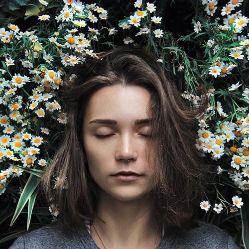 Photo of a girl lying down, eyes closed, in a bed of flowers - Ann Danilina on Unsplash