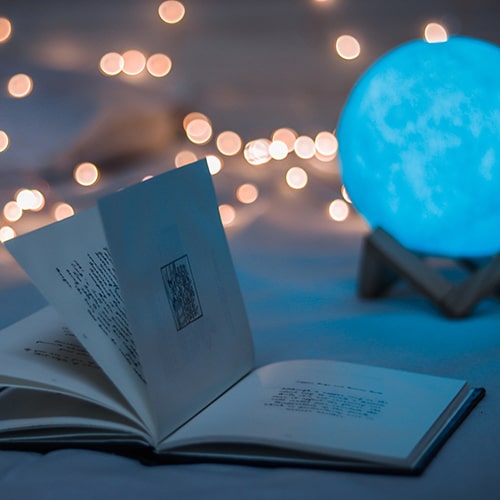 Photo of an open book on a bed with a moon light with bokeh lights in the background - Dollar Gill on Unsplash