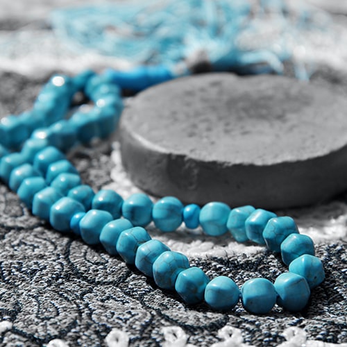 Focused shot of turqouise blue beads next to a grey stone, lying on top of a black and white mat/rug - Hasan Almasi on Unsplash