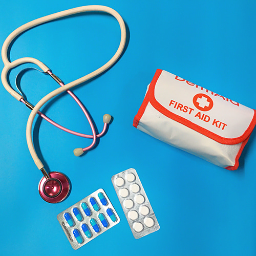 Photo of medical supplies (stethoscope, First Aid Kid, and two packets of sealed pills and tablets) on a rich, turqouise blue background - Kristine Wook on Unsplash