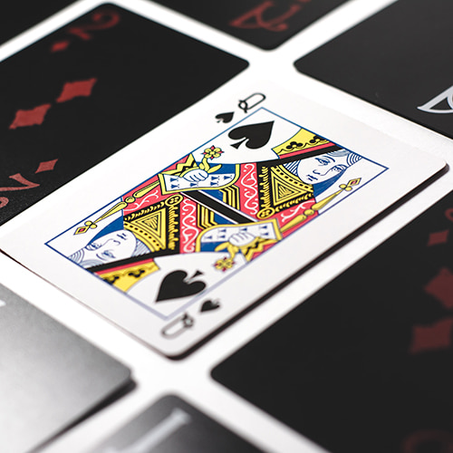 Photo of a Queen of Spades card amongst red and white numbered/Ace cards on black - Esteban Lopez on Unsplash