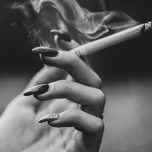 Zoomed-in black and white photo of a woman with long, painted nails holding a smoking cigarette - Anastasia Vityukova on Unsplash