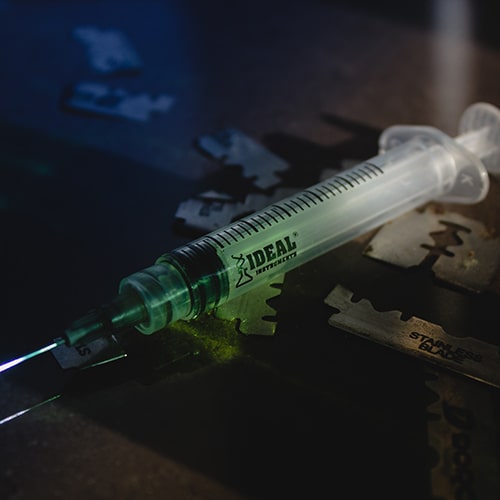 Zoomed-in shot of a white and green Ideal Instruments syringe on a wodden counter with Stainless Blades scattered about - abyss on Unsplash