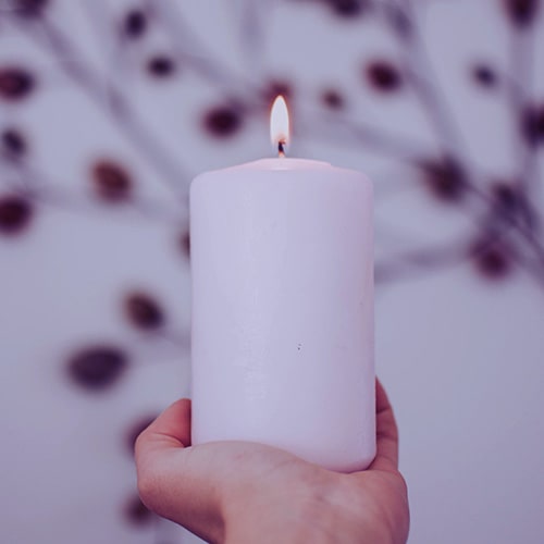 Image of a hand holding a candle with a burning wick with a blurred, decorative background - fotografierende on Unsplash (edited by me)