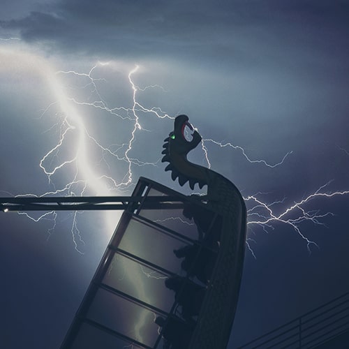 Photo of a stormscape with vein lightning in the background with a dragon boat carnival/fair/amusement park ride with passengers in the foreground - haik ourfal on Unsplash