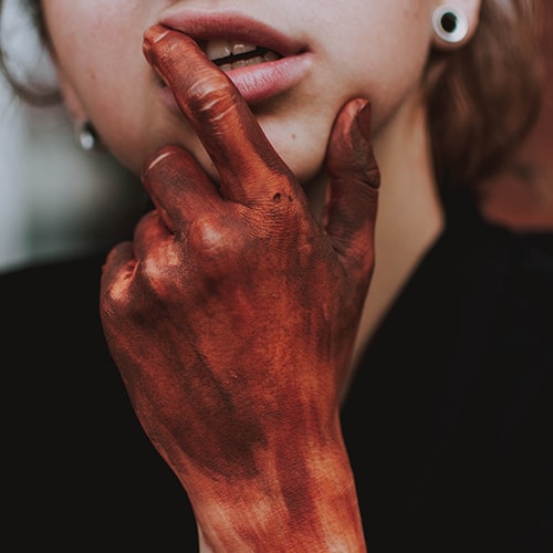 Close-up shot of a woman holding her hand up to her face with red paint made to look like blood on her hand - fotografierende on Unsplash