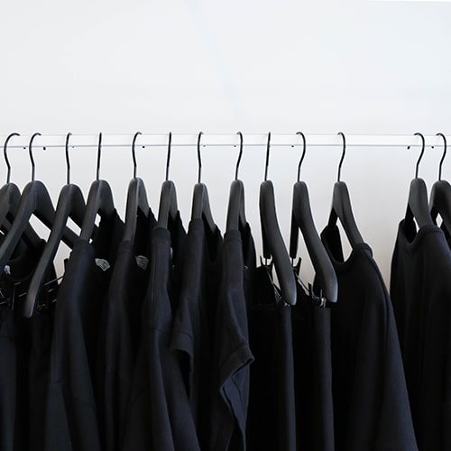 Photo of black clothes hanging on black hangars on a white clothing rack against a white wall - The Creative Exchange on Unsplash