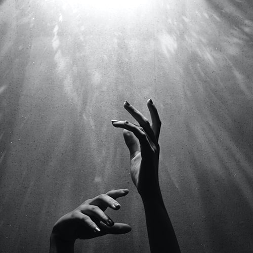 Black and white photo of a woman's hands reaching up towards a bright light - I.am_nah on Unsplash