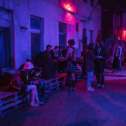 Photo of people standing and sitting on wooden pallets outside of a concrete building