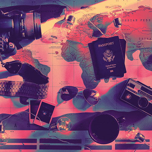 Photo of a map of the world with things like a string of light bulbs, a Passport or two, cameras, and a pair of aviator sunglasses lying on top of it
