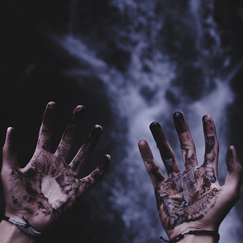 Photo of a pair of hands, palms up, covered in a liquid/paint that's meant to resemble blood, against a blurred/unfocuse waterfall background - Ian on Unsplash