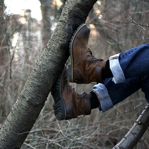 Photo of someone's legs in cuffed jeans, black socks, and dark Timberland boots bent and pressed up against a tree