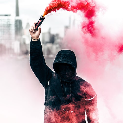 Photo of a faceless man holding up a red smoke canister, with smoke from the canister flowing around him - Warren Wong on Unsplash