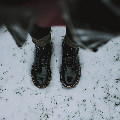 Bird's-eye, top-down photo of a person in a jacket, red top, dark jeans, leg warmer socks, and a pair of leather boots standing on snowy ground - fotografierende on Unsplash