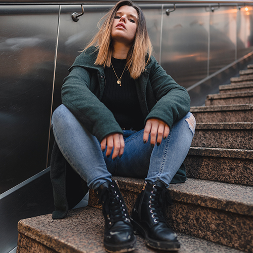 Photo of a woman with a chocolate-brown to golden blonde ombré sitting and posing on a set of stone/marble stairs against a steel wall - Philipp Lansing on Unsplash