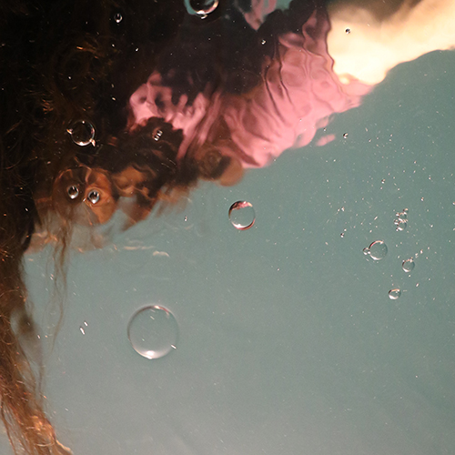 Abstract, distorted photo of someone with red hair in a pink shirt submerged underwater - Serenity Mitchell on Unsplash